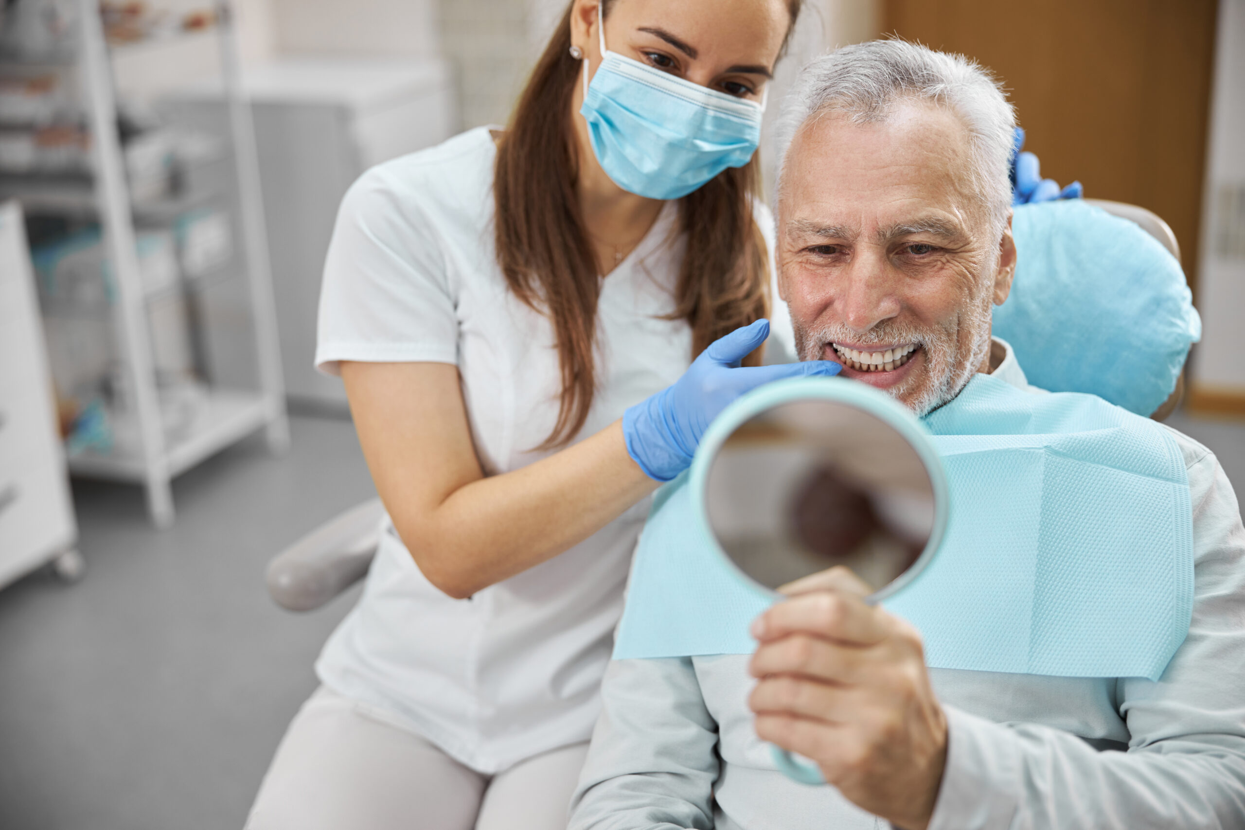 Aging gentleman being happy with his new dental implant Elderly man and his young female dentist smiling while looking in the mirror in dental clinic