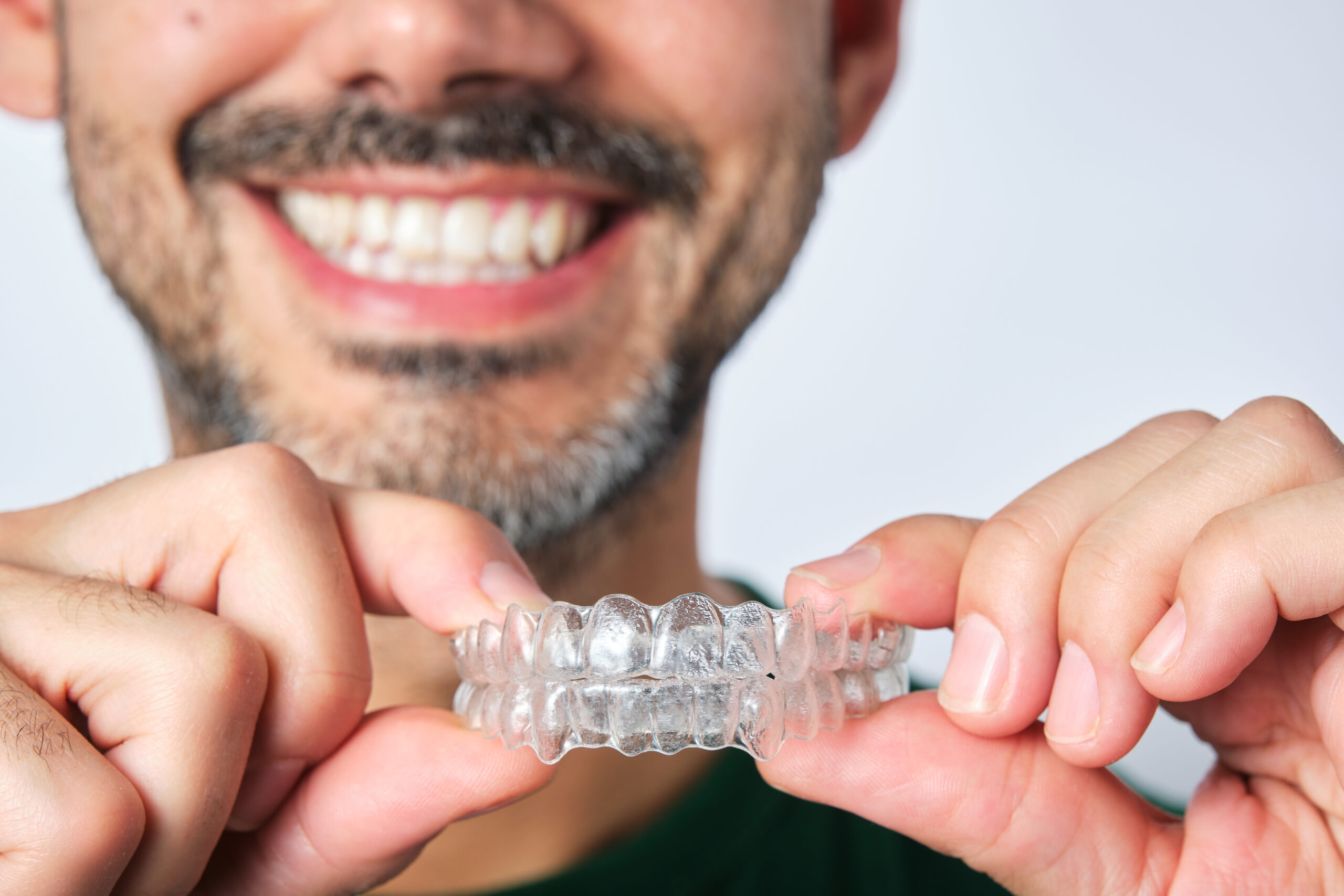 man with transparent dental retainer closeup man hand holding transparent retainer with unrecognizable bearded man face in unfocused background on white background