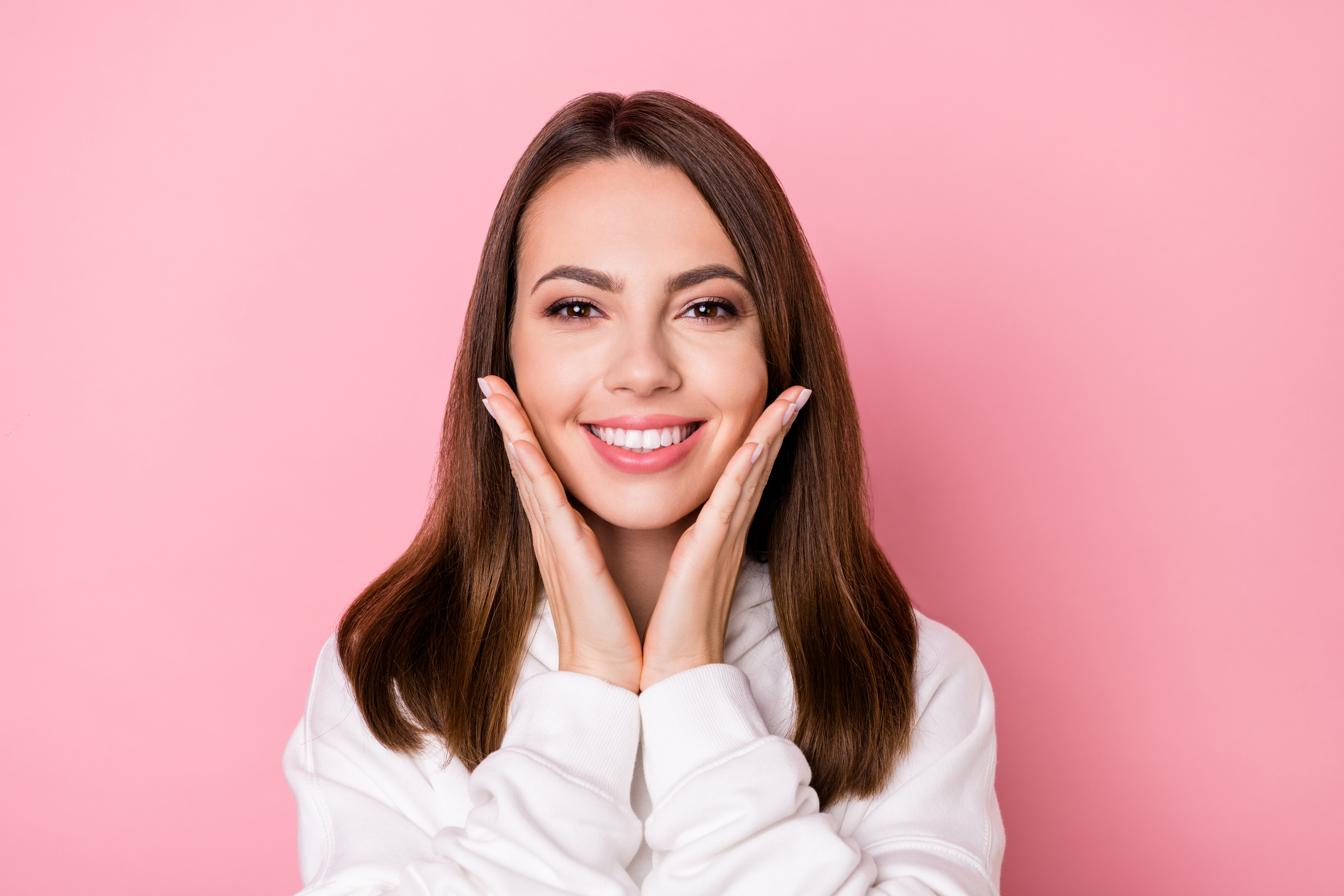 Photo of attractive happy young pretty woman hold hands face cheeks teeth isolated on pink color background Photo of attractive happy young pretty woman hold hands face cheeks teeth isolated on pink color background.