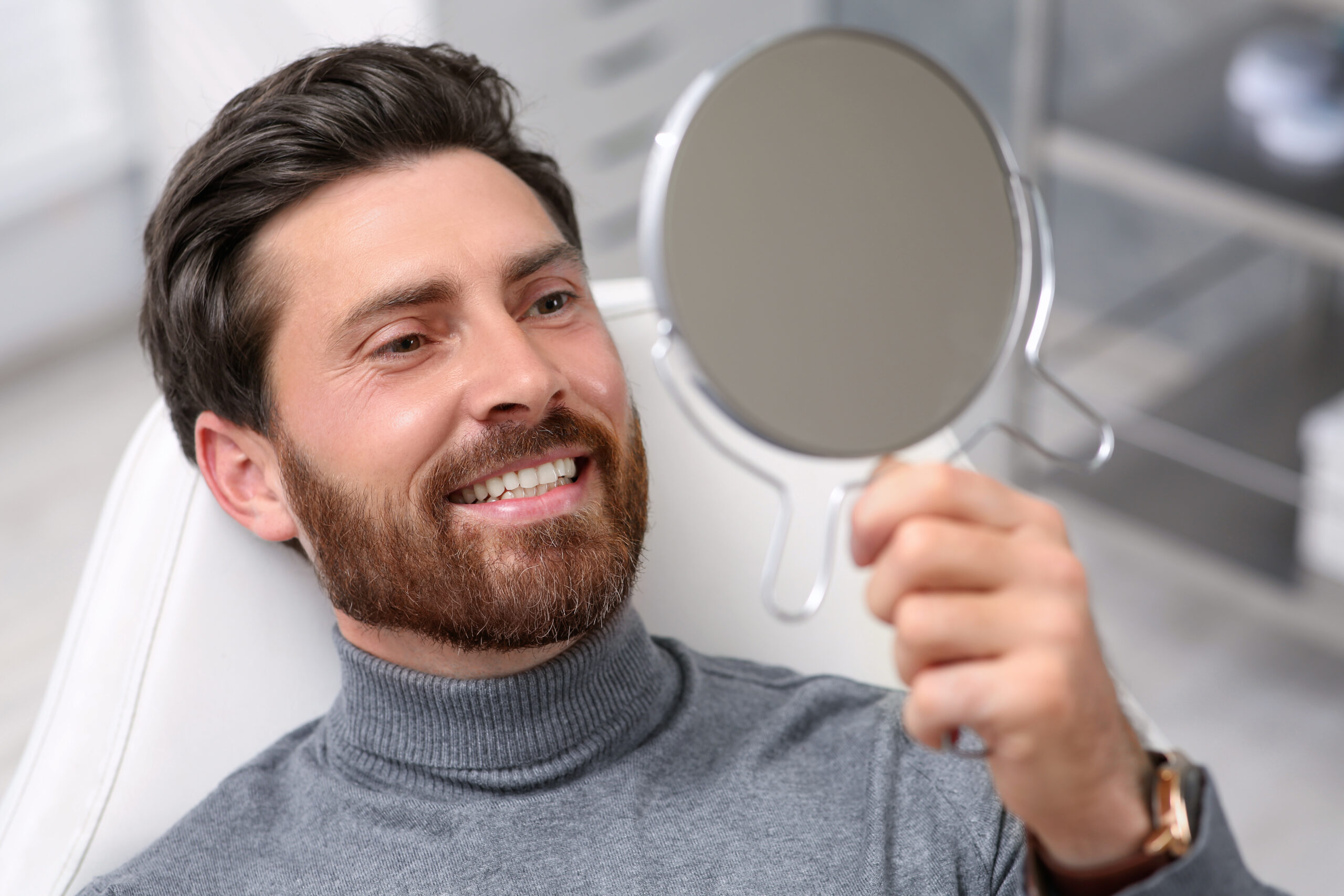 Man looking at his new dental implants in mirror indoors Man looking at his new dental implants in mirror indoors
