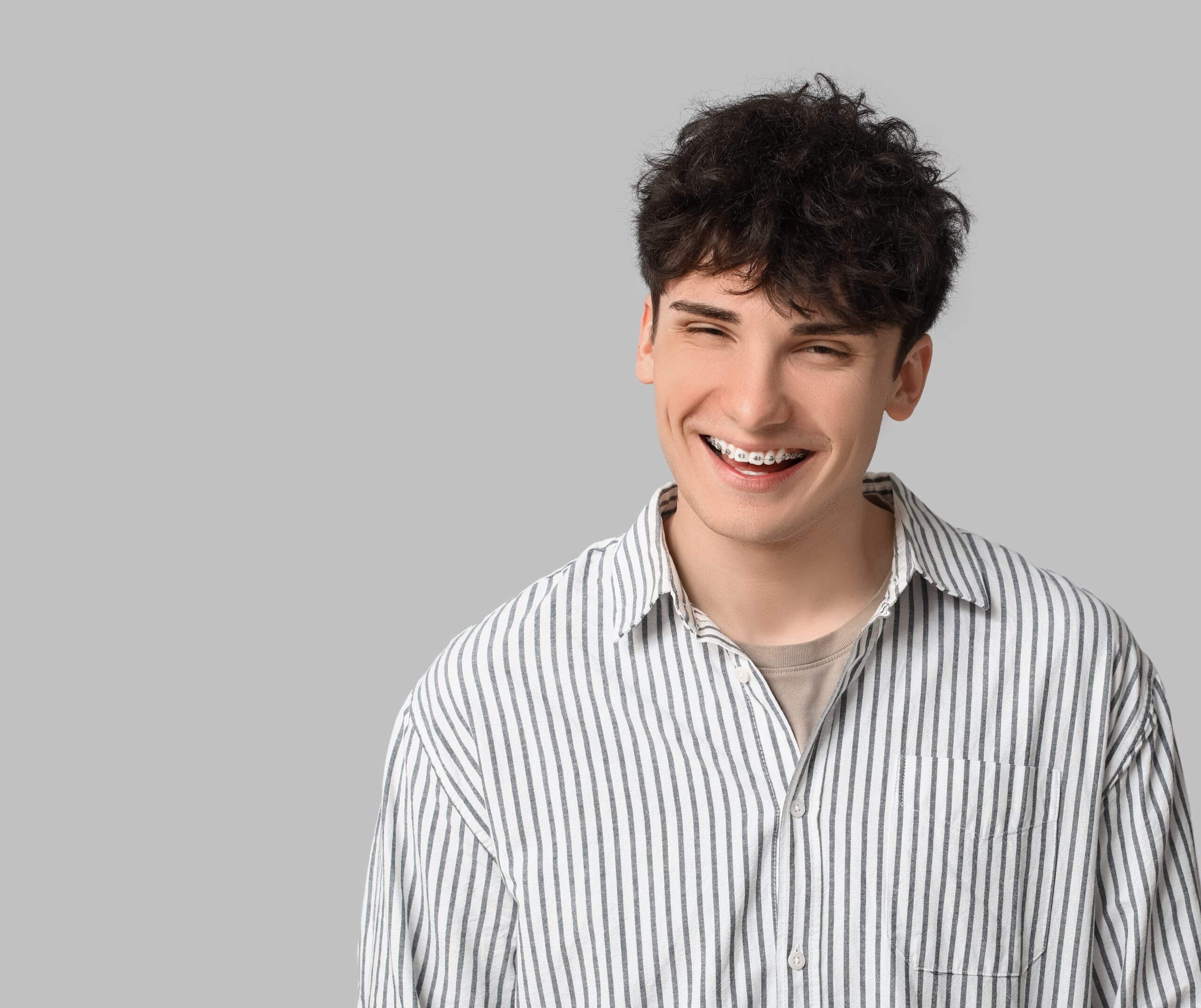 Smiling young man with dental braces on light background Smiling young man with dental braces on light background