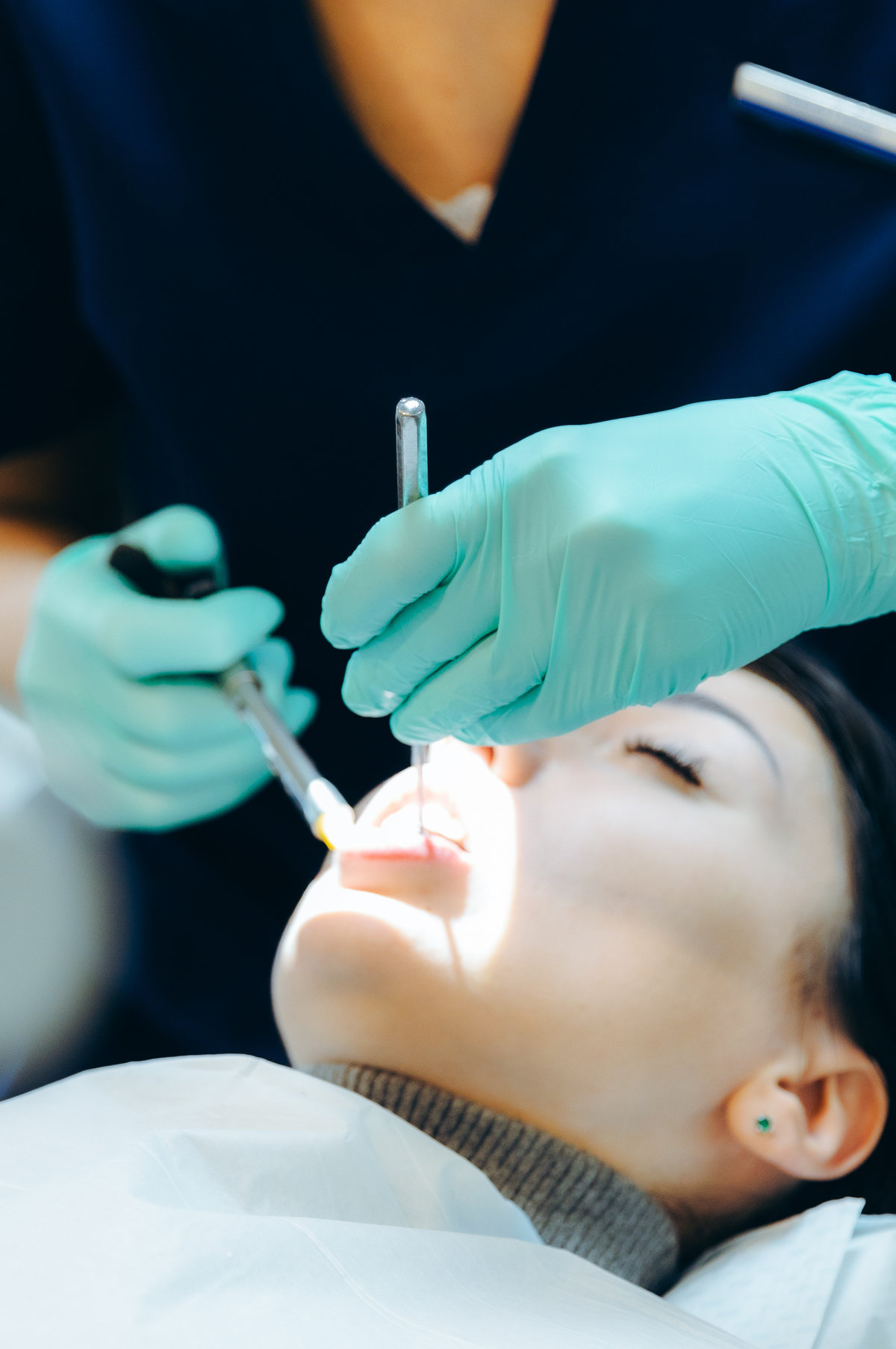 A dentist gives an anesthesia injection to a patient in a dental home. An unrecognizable Caucasian dentist in green latex gloves gives an anesthesia injection to a girl patient using a disposable syringe and a dental mirror in a private clinic, side view very close-up. Concept for treatment of gums and teeth, dentist's day.